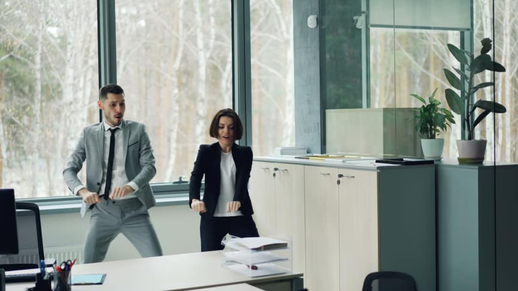 Two adults dance in a modern office space with large windows-The Ultimate Desk Workout Hack Everyone's Talking About