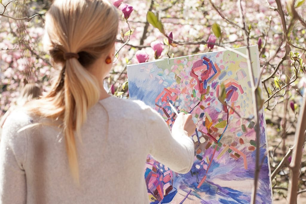 woman in white long sleeve shirt holding white and blue floral painting showing one of the 10 fascinating types of intelligence you need to know