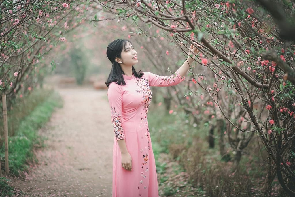 A woman in a pink dress stands gracefully among blossoming trees, embodying beauty and tradition. She is enjoying the amazing healing power of nature you should know too