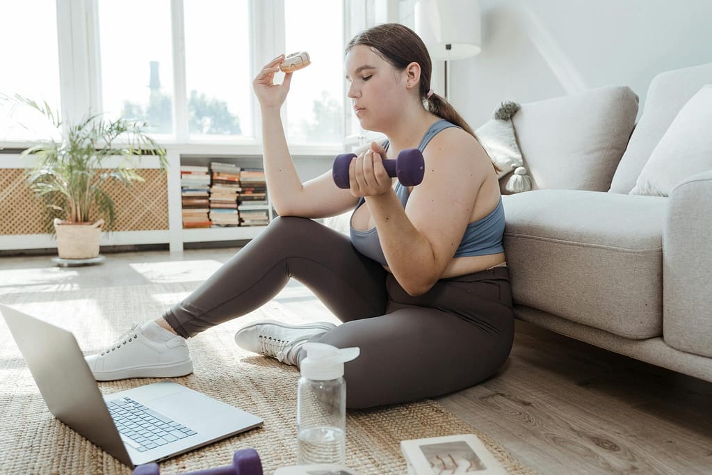 A woman enjoys a donut while exercising at home, promoting balance and body positivity.