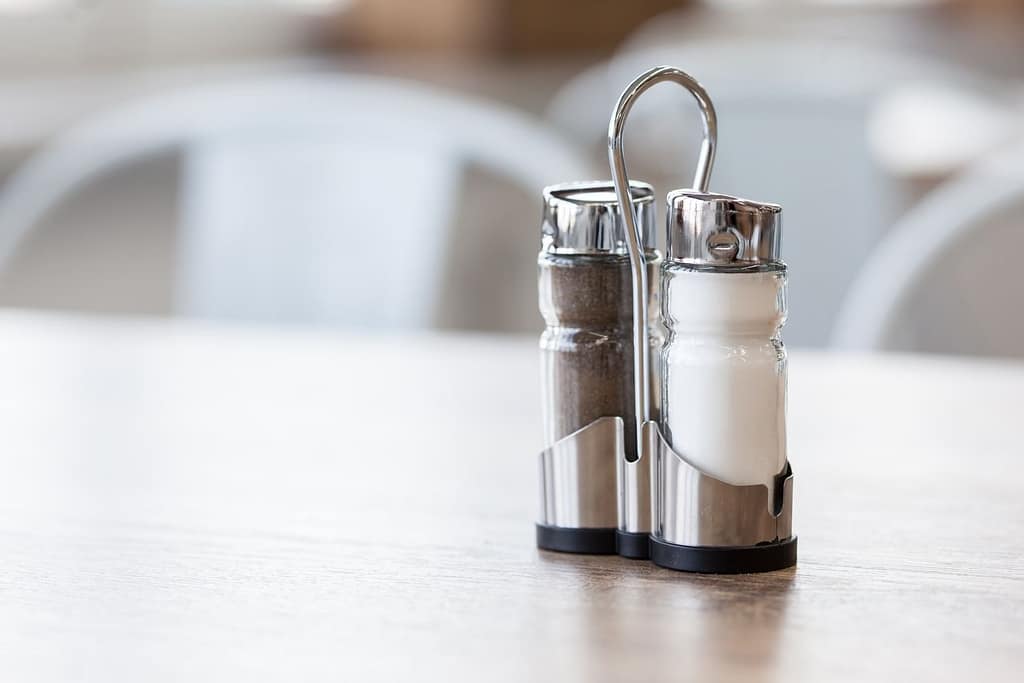 Salt and ground black pepper shakers in stainless steel holder on table in restaurant on blurred background