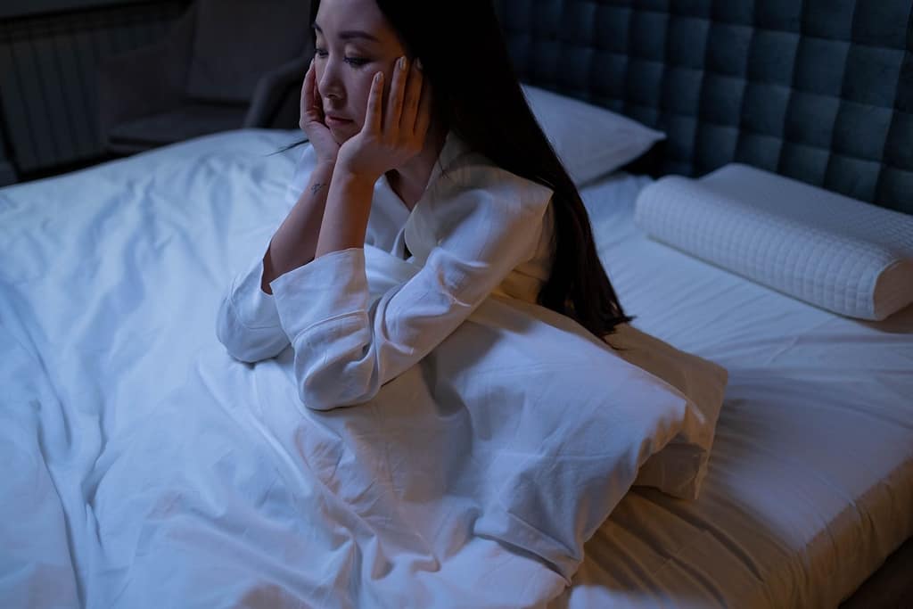 An Asian woman in bed at night, experiencing insomnia and loneliness, deep in thought-Proven Ways to Crush Stress Belly Fat for Good