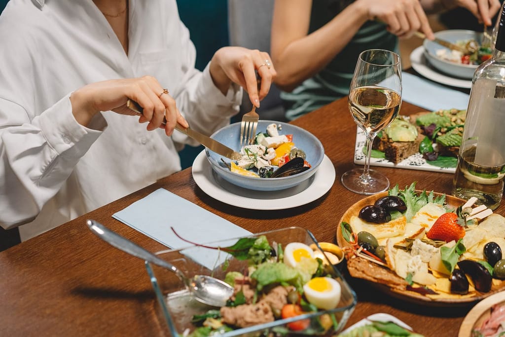 Elegant dining setting featuring fresh salad, dishes, and white wine, capturing a social gathering ambiance.
