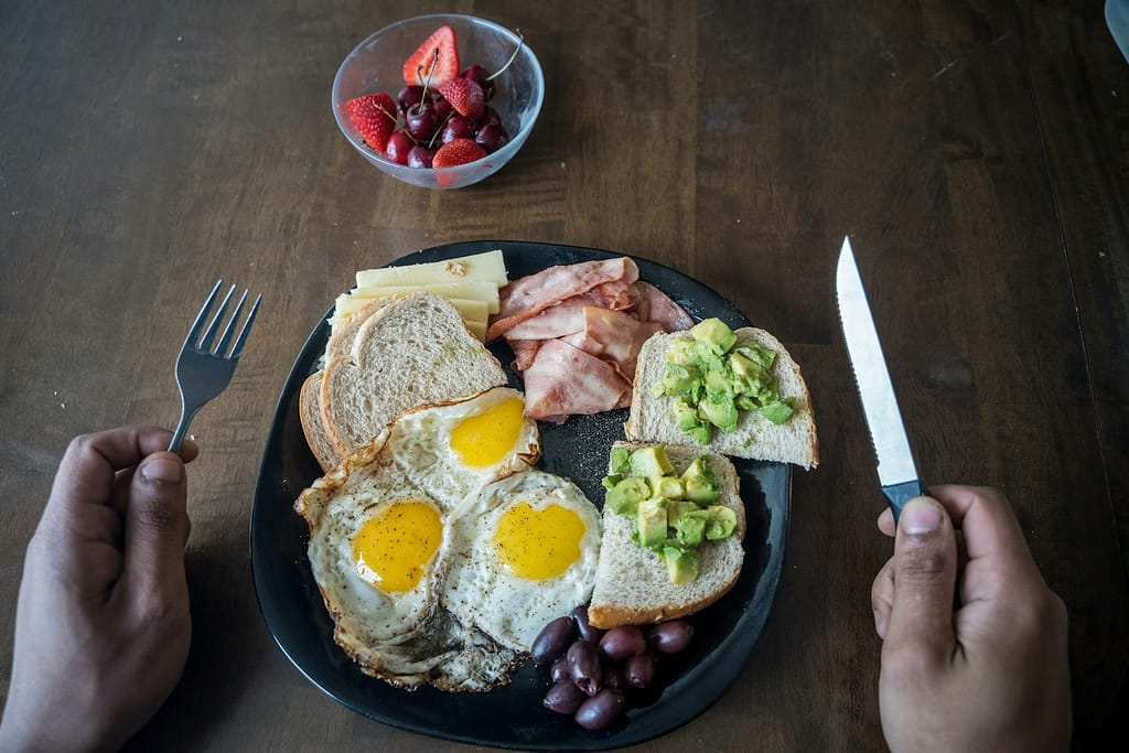 sliced bread with sliced tomato and cucumber and eggs on black ceramic plate