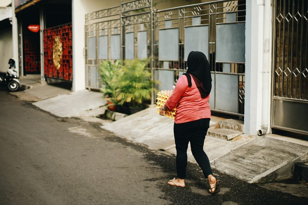 woman in black and red jacket and black pants walking on sidewalk during daytime