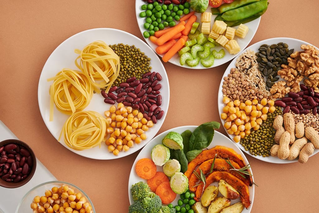 A vibrant mix of legumes, vegetables, nuts, and pasta arranged on white plates showcasing a balanced, healthy diet-Fiber: The Most Important Nutrient Nobody’s Talking About.