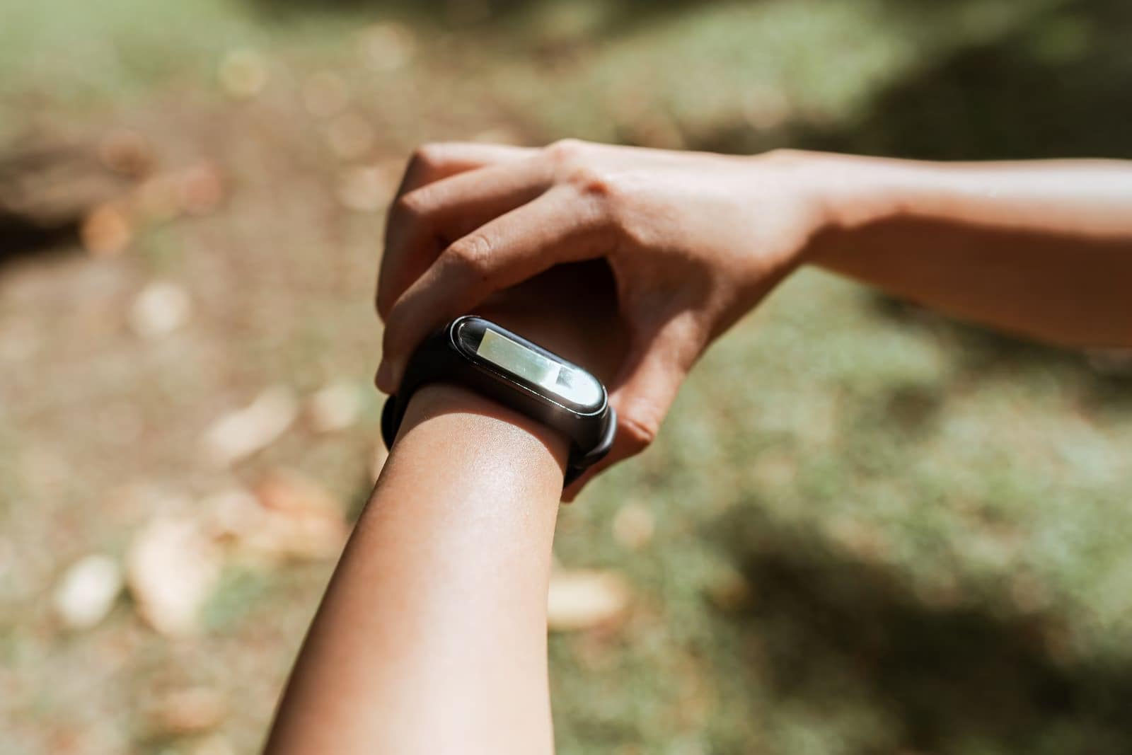 Crop unrecognizable female checking notifications on hand fitness tracker while exercising on green lawn on sunny summer day-The Shocking Truth About $80 Fitness Trackers You Didn't Know