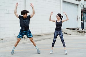 a man a woman doing jumping jacks exercise outdoors