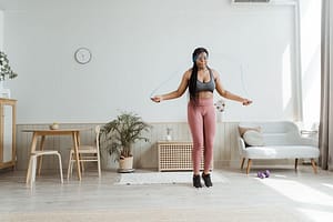 Confident black woman in activewear jump roping at home, promoting wellness and body positivity.