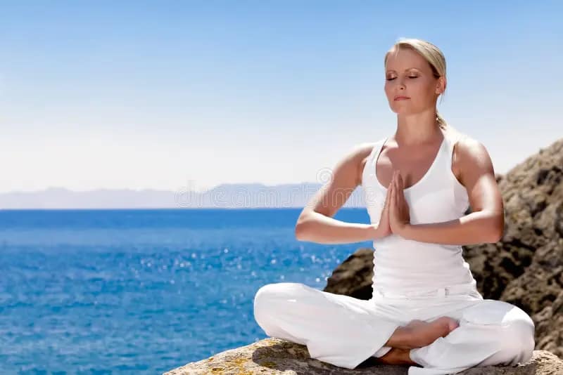 A woman in white doing yoga beside the sea